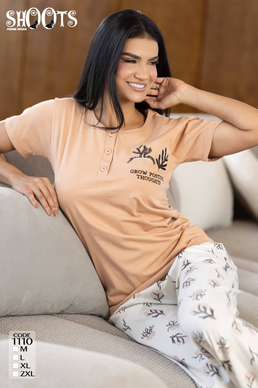 Woman wearing a peach-colored polo shirt with text and white pants with black patterns, sitting on a beige couch.